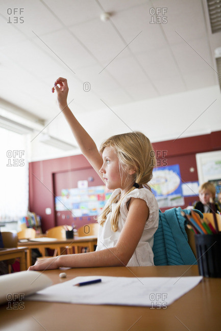 Schoolgirl raising hand in classroom stock photo - OFFSET