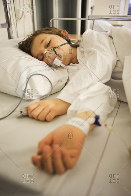 Girl lying on hospital bed with oxygen mask over face stock photo - OFFSET