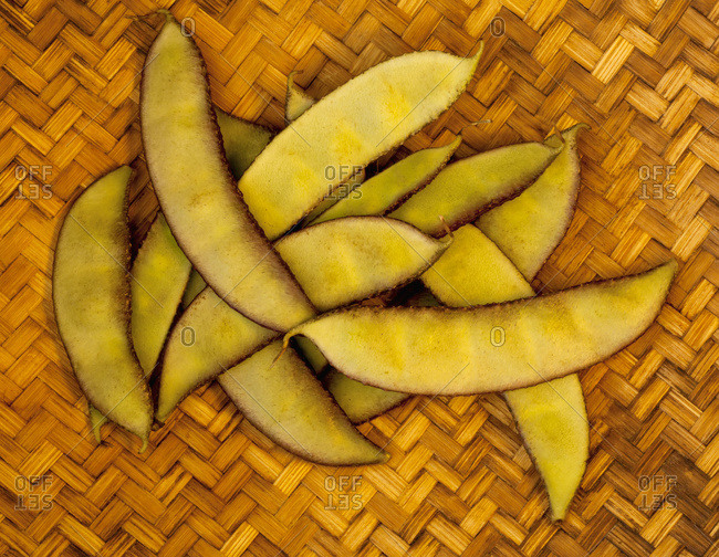 A handful of a tropical variety of peapods from a local farmers market rest on a woven mat on the Big Island; Pahoa, Island of Hawaii, Hawaii, United States of America
