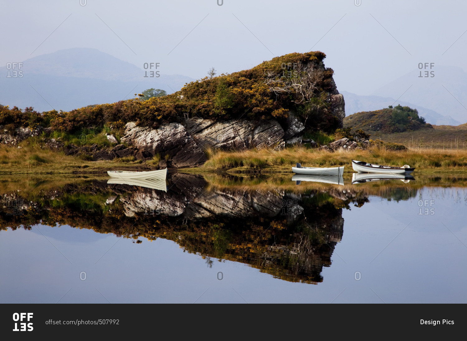Canoes moored along the shoreline with a mirror image of a rugged cliff reflected in the water in Killarney National Park; County Kerry, Ireland
