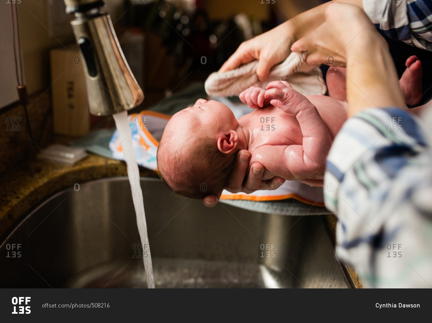 Parents rinsing baby\'s head at a sink