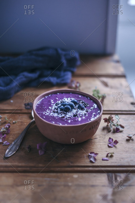 Blueberry acai smoothie bowl topped with blueberries, shredded coconut and cacao nibs on rustic wooden table