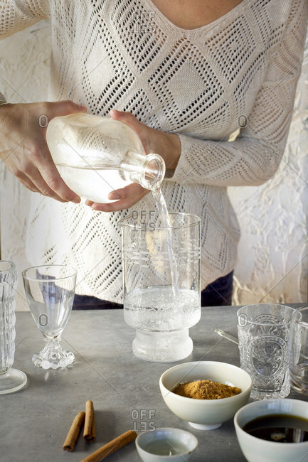 A Women is pouring Sparkling Water into glassware. Photographed on dark gray background.