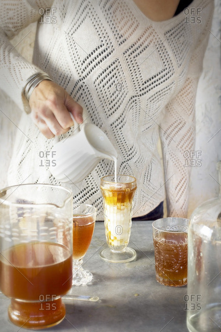 A Women is pouring cream into Almond Lime Italian Soda in glassware. Photographed on dark gray background.