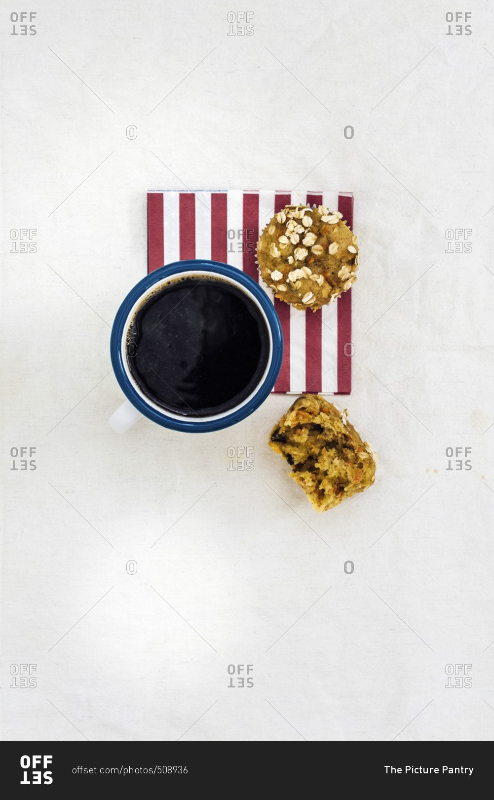 A mug of coffee and a carrot muffin on a red striped napkin photographed from top view. Half of a muffin is on the side.