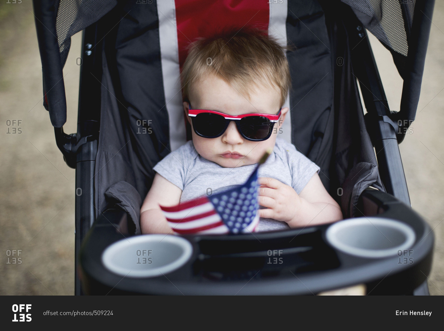 Baby boy with sunglasses in a stroller holding an American flag