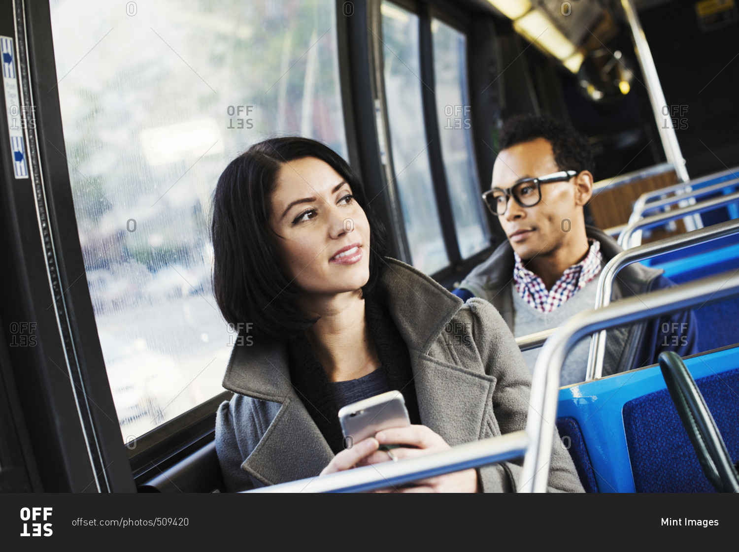 A young man and a young woman sitting on public transport holding their cellphones and looking around