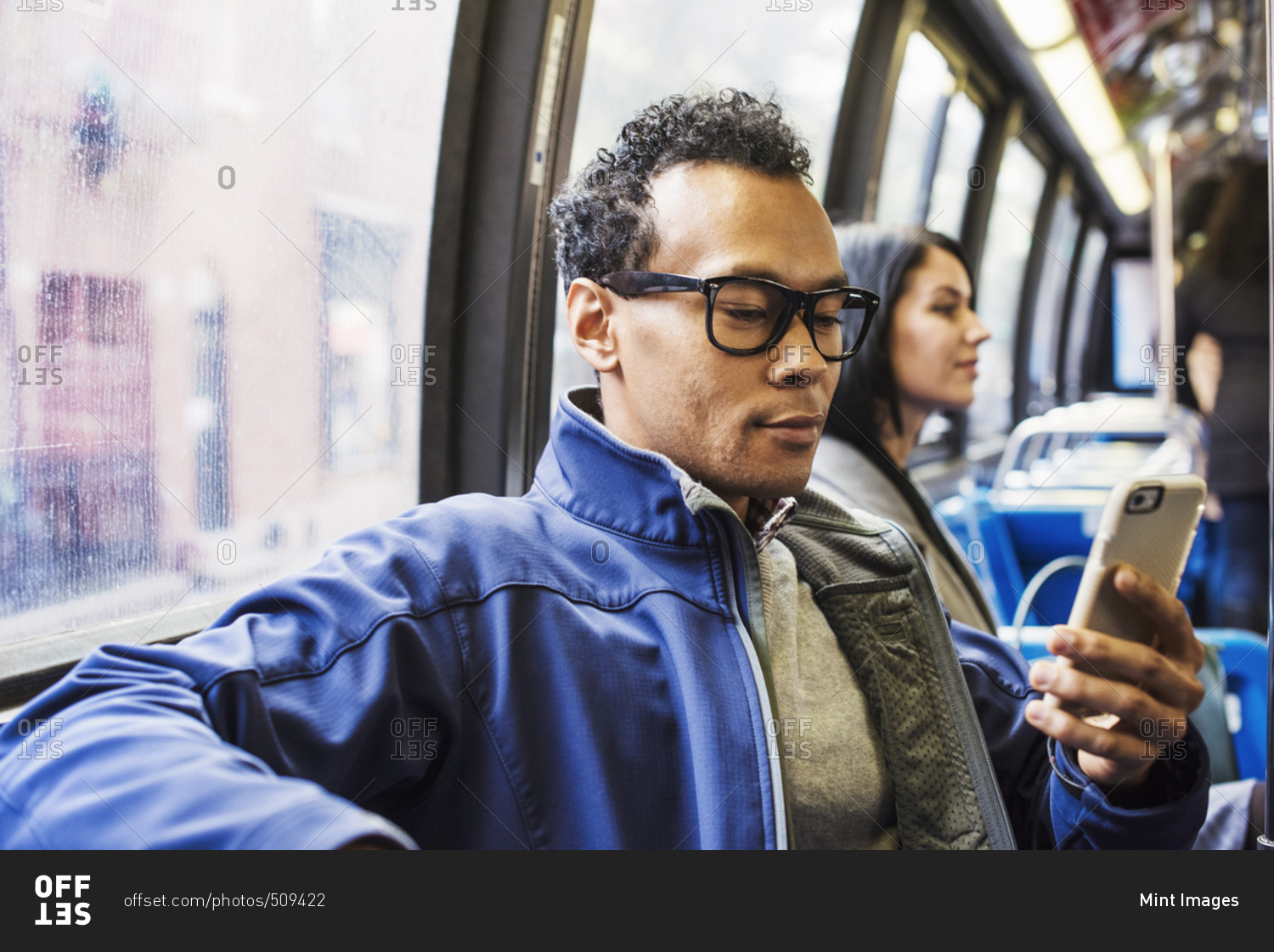 A young man and a young woman sitting on public transport looking at their cellphones