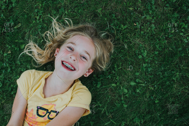 Little girl with braces lying on a lawn grinning