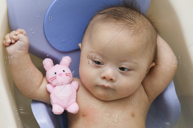 Mixed race Down Syndrome baby laying in plastic bathtub