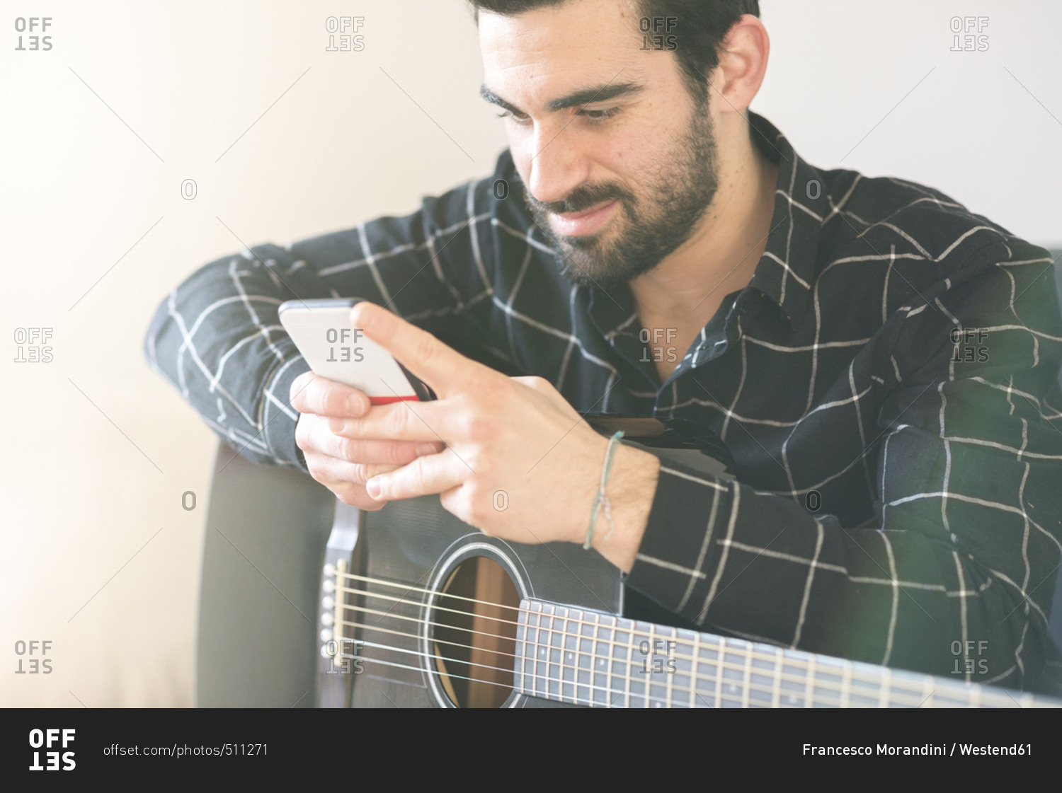 Young man at home with guitar and cell phone