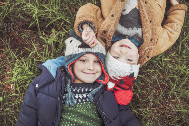 Two boys wearing wooly hats lying in grass