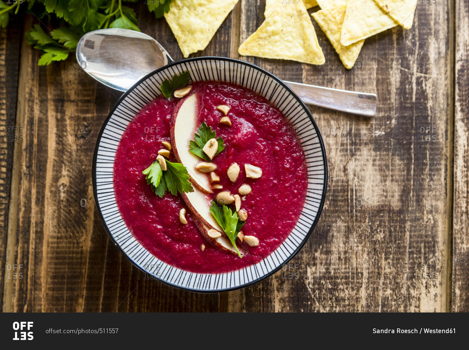 Bowl of beetroot soup garnished with apple slices- peanuts and flat leaf parsley served with tortilla chips