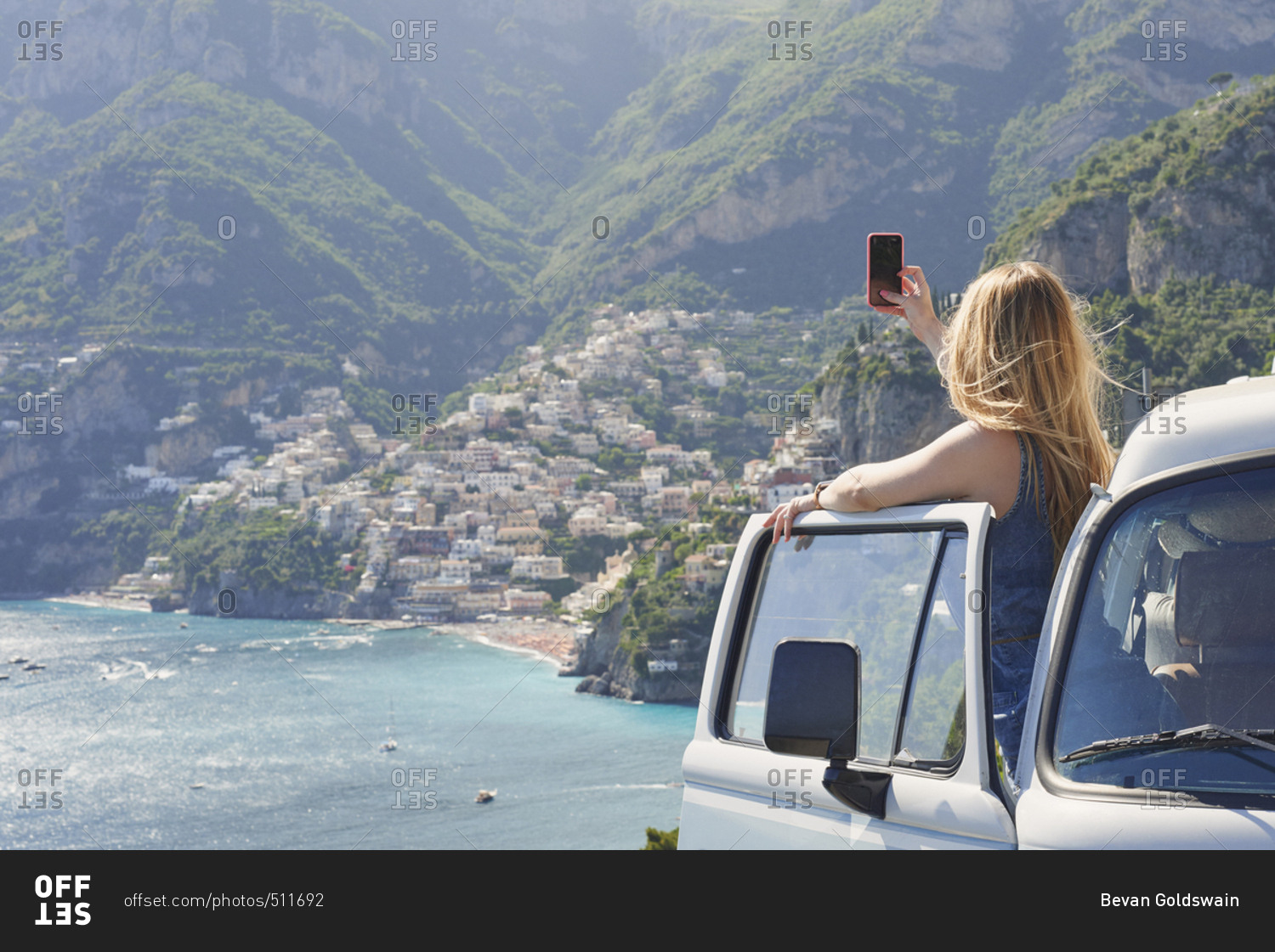 Beautiful girl takes photograph of coast on road trip using smart phone technology for social media while on adventure travel vacation