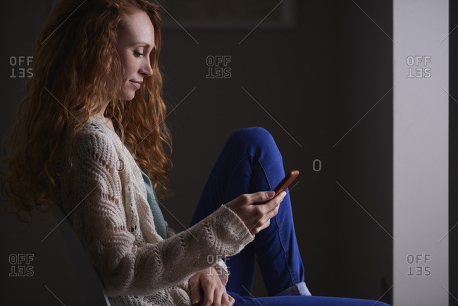 August 1, 2016: Beautiful redhead woman using smart phone technology at home browsing network internet social media