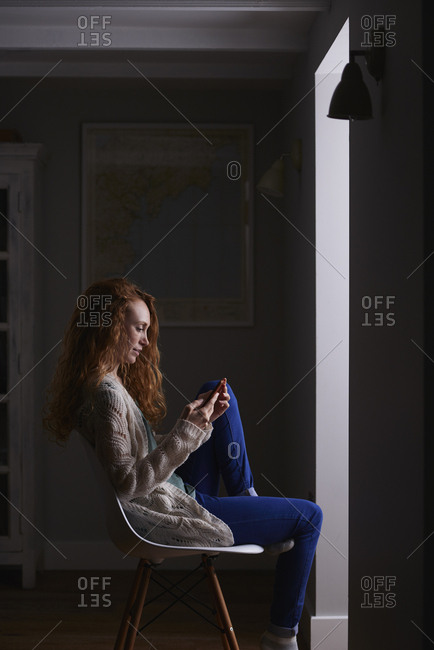 August 1, 2016: Beautiful redhead woman using smart phone technology at home browsing network internet social media