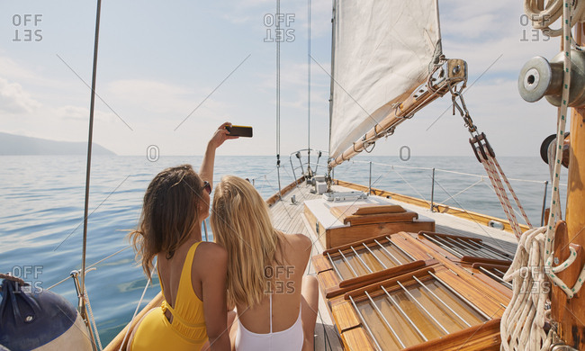 Beautiful women friends taking selfies smart phone social media on sailboat in ocean on luxury lifestyle adventure travel vacation