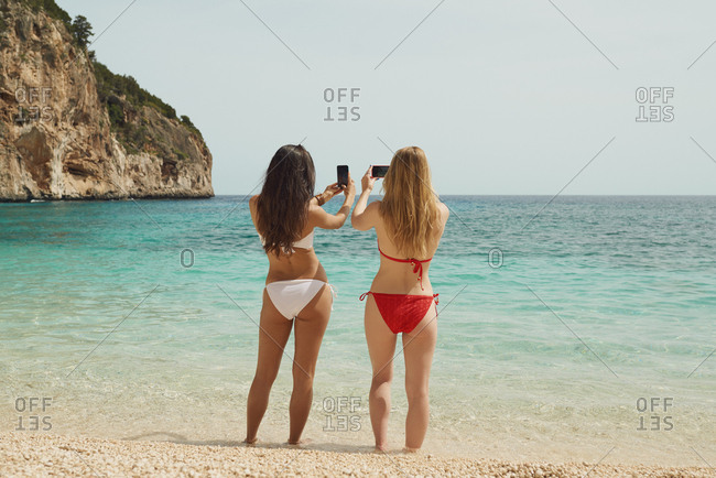 Beautiful girl friends taking photos with smart phone technology on paradise beach destination summer wanderlust vacation
