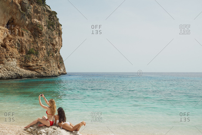 Beautiful girl friends taking selfies with smart phone technology on paradise beach destination summer wanderlust vacation