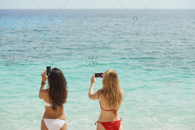 Beautiful girl friends taking photos with smart phone technology on paradise beach destination summer wanderlust vacation