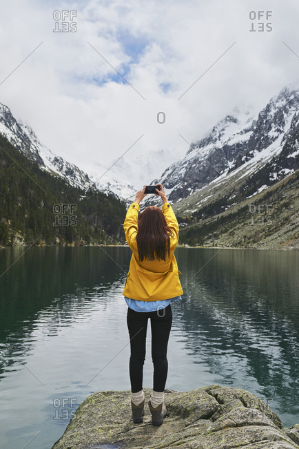 Travel adventure woman taking smart phone photograph on mountain lake enjoying beautiful nature landscape wanderlust