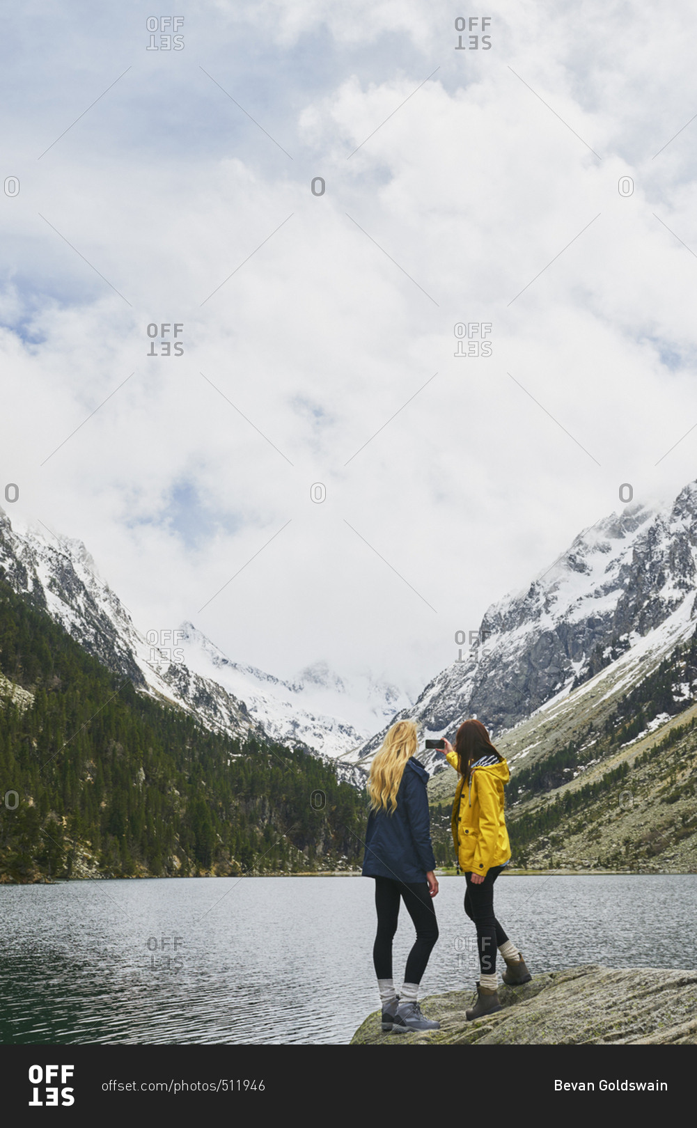 Travel adventure woman friends taking smart phone photograph on mountain lake enjoying beautiful nature landscape wanderlust