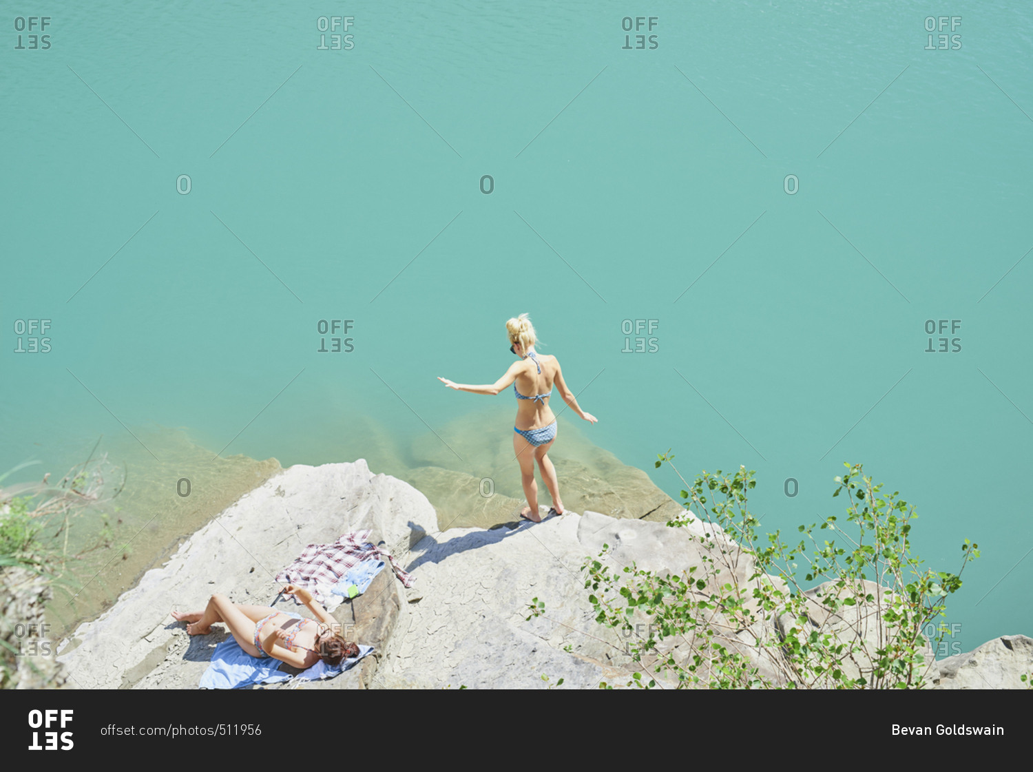 Beautiful girl friends testing water to wild swim in beautiful blue freshwater river on summer adventure vacation in nature