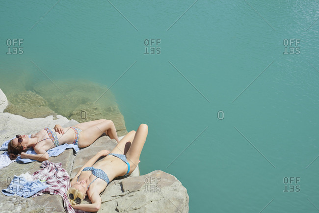 Beautiful girl friends tanning to wild swim in beautiful blue freshwater river on summer adventure vacation in nature