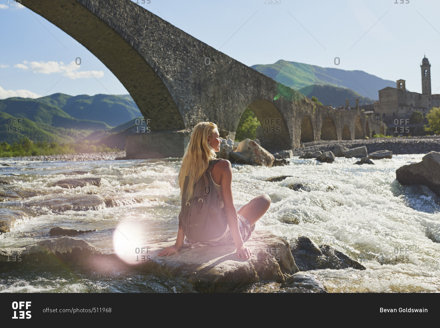 Travel adventure woman sitting on rock in river enjoying scenery view historical european town