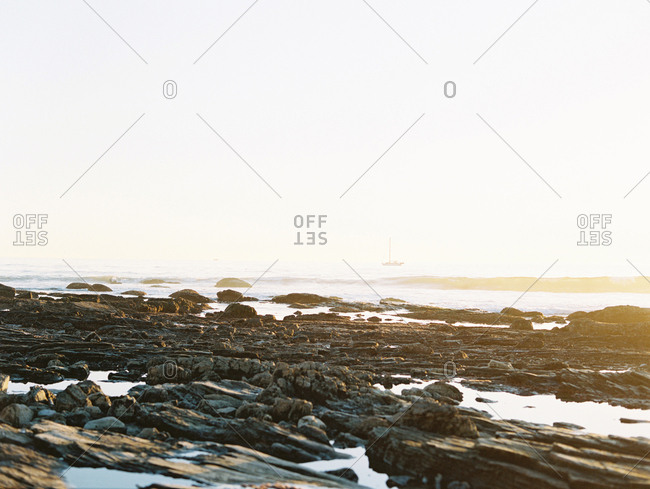 Rocky shore and a distant boat at sunset