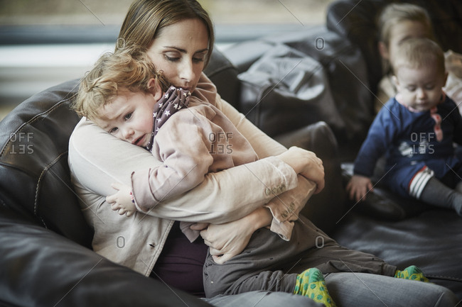 Mother consoling daughter on couch with siblings in background