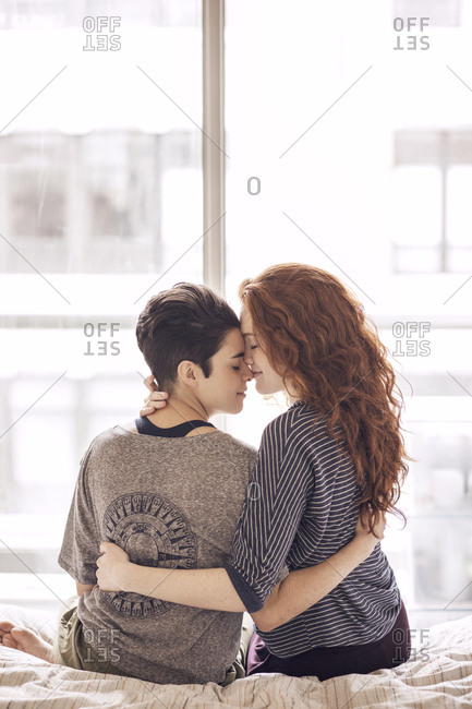 Lesbian couple romancing while sitting on bed at home
