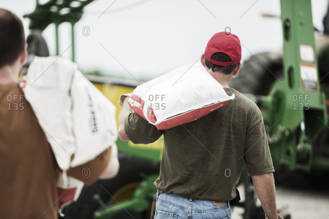 Rear view of men carrying gunny bags against machinery at farm