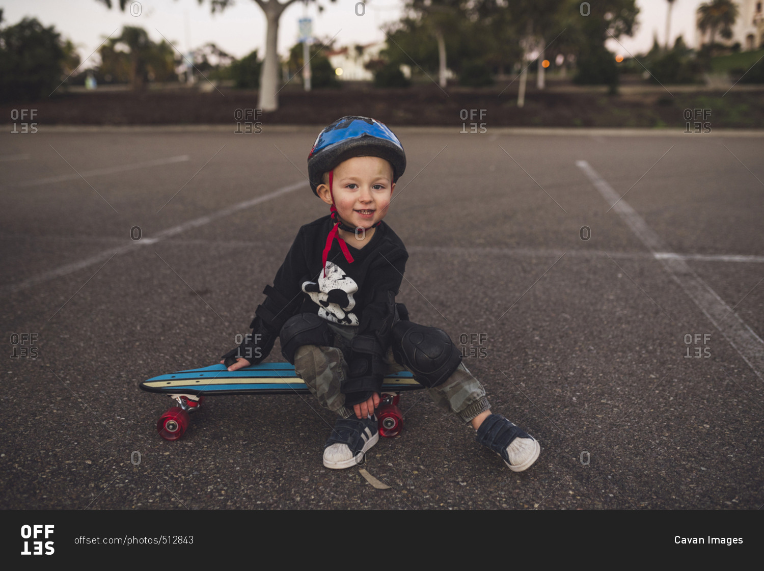 Portrait of cute boy sitting on skateboard at field