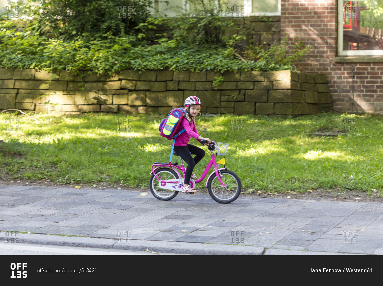 Smiling little girl with school bag riding bicycle on pavement