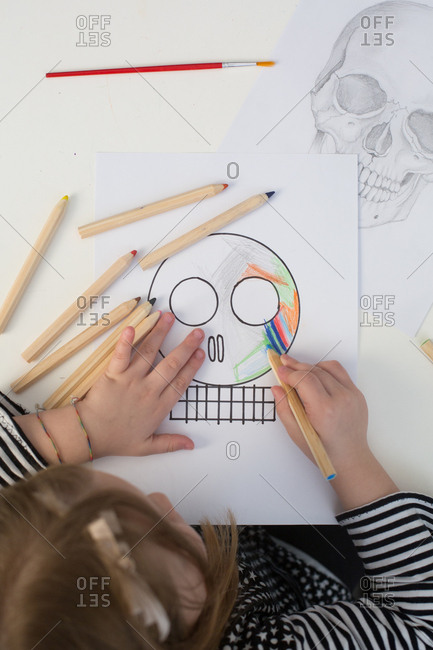 Girl coloring a simple sketch of a skull with a realistic skull at the background