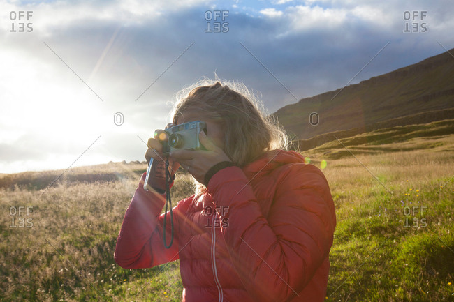 Female tourist photographing from sunlit hillside, Seyoisfjorour, Iceland