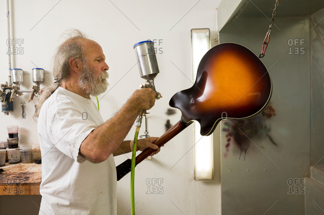 Guitar maker in workshop using spray gun to varnish guitar