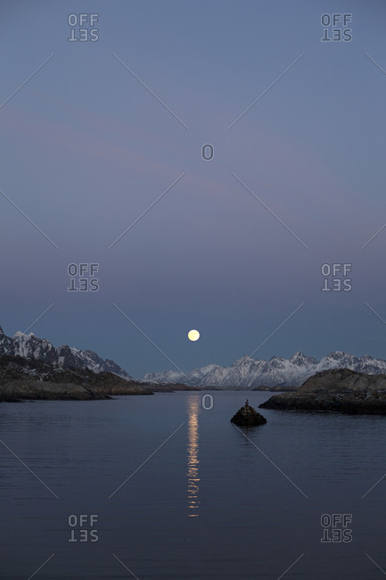 Moon rising over the water and distant mountains in Kabelvag, Norway