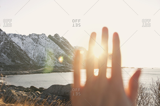 Hand blocking out the sun with a view of distant mountains and water
