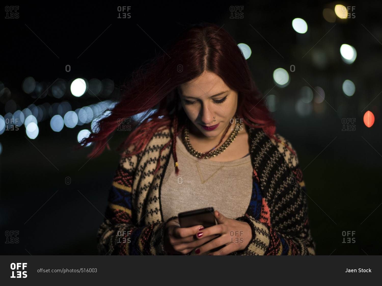 Red haired woman on her phone with night lights in the background