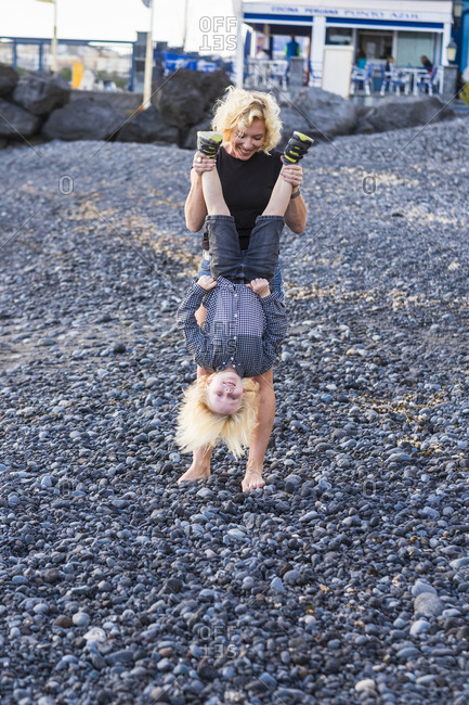 Woman on beach holding boy upside down