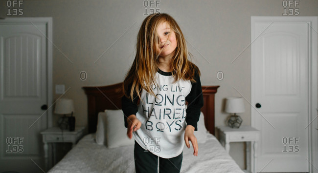 Long-haired boy playing on bed stock photo - OFFSET