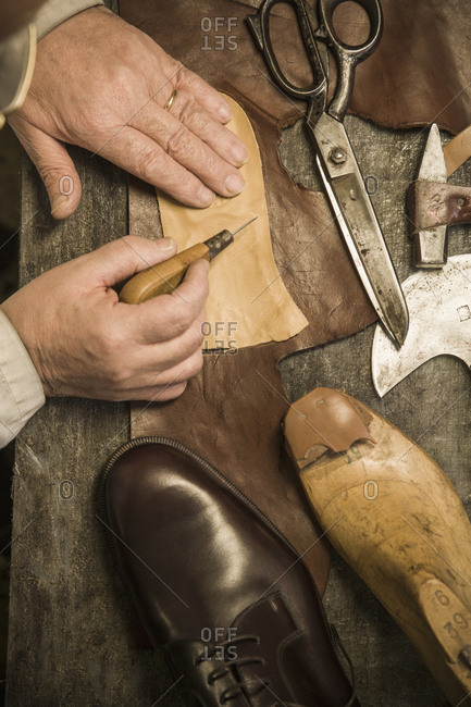 Hands of shoemaker using awl on leather