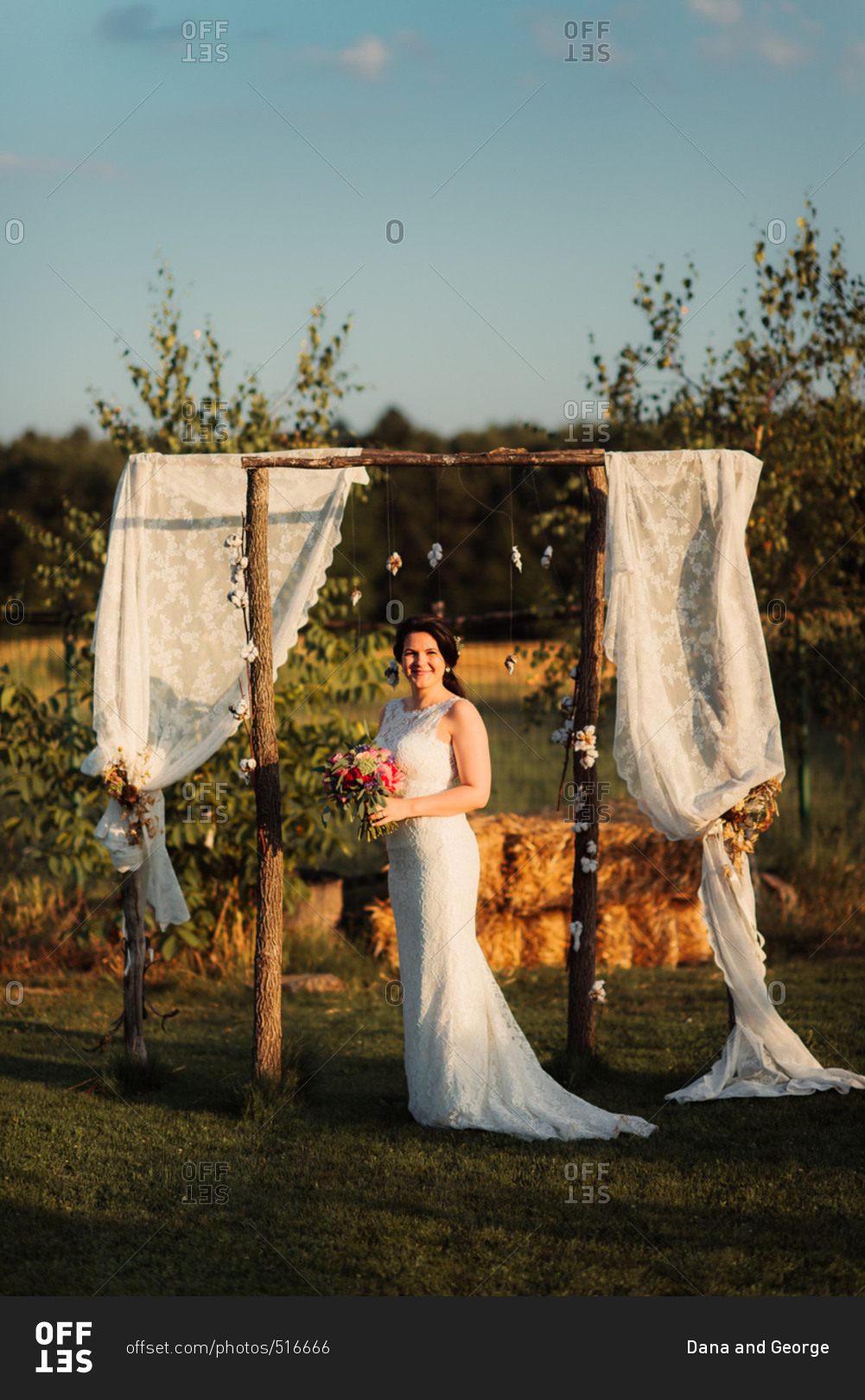 Happy bride standing under wedding arbor in the countryside