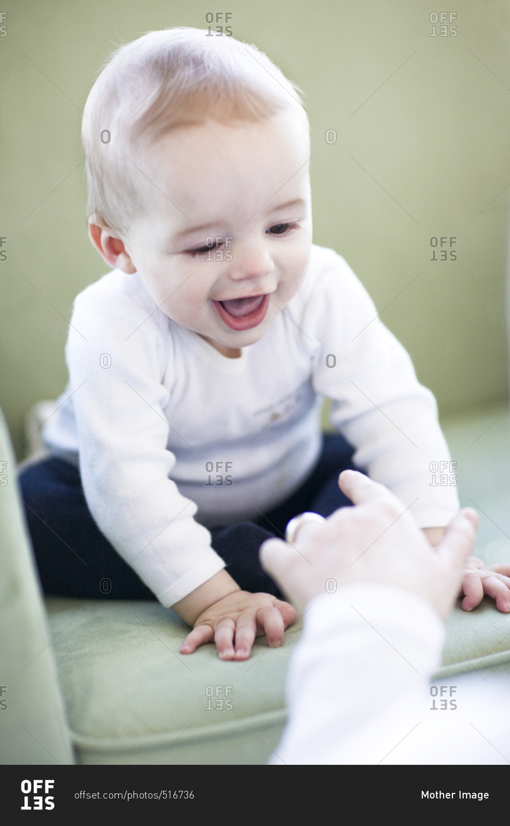 Baby boy smiling on rocking chair playing with adult poking finger at him