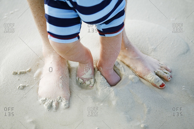 Baby boy feet and moms feet covered in sand on beach