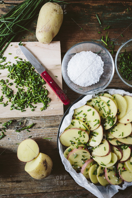 Slices of potatoes with chives- red peppercorns and salt in baking pan