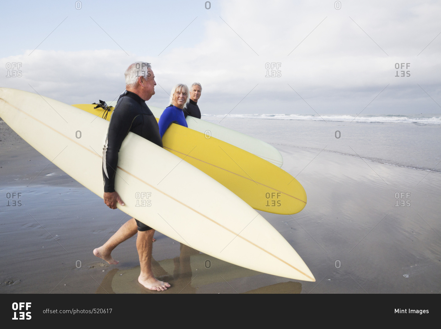 Senior woman and two senior men on a beach, wearing wetsuits and