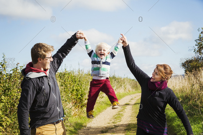 Parents holding a small boy's hands and lifting him up in the air.